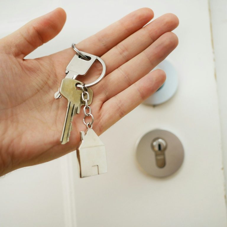 Hand mit Haustürschlüsseln und einem Schlüsselanhänger in Form eines Hauses.